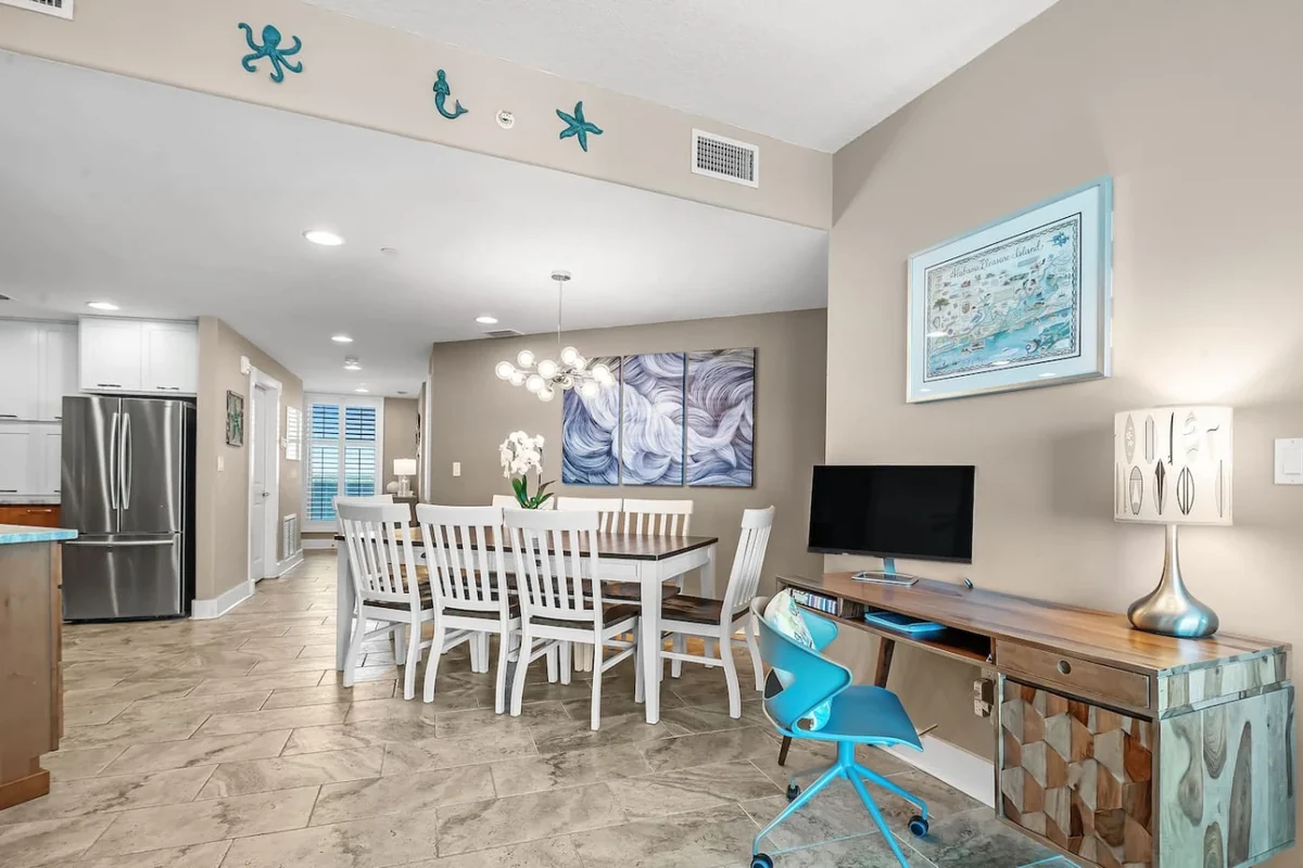Gulf Shores dining room with a long white table, coastal artwork and the open kitchen beyond