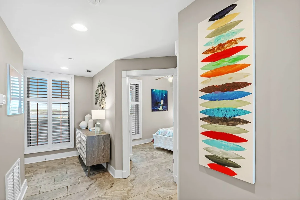 Gulf Shores condo entry hall with plantation shutters, a console and colorful coastal artwork